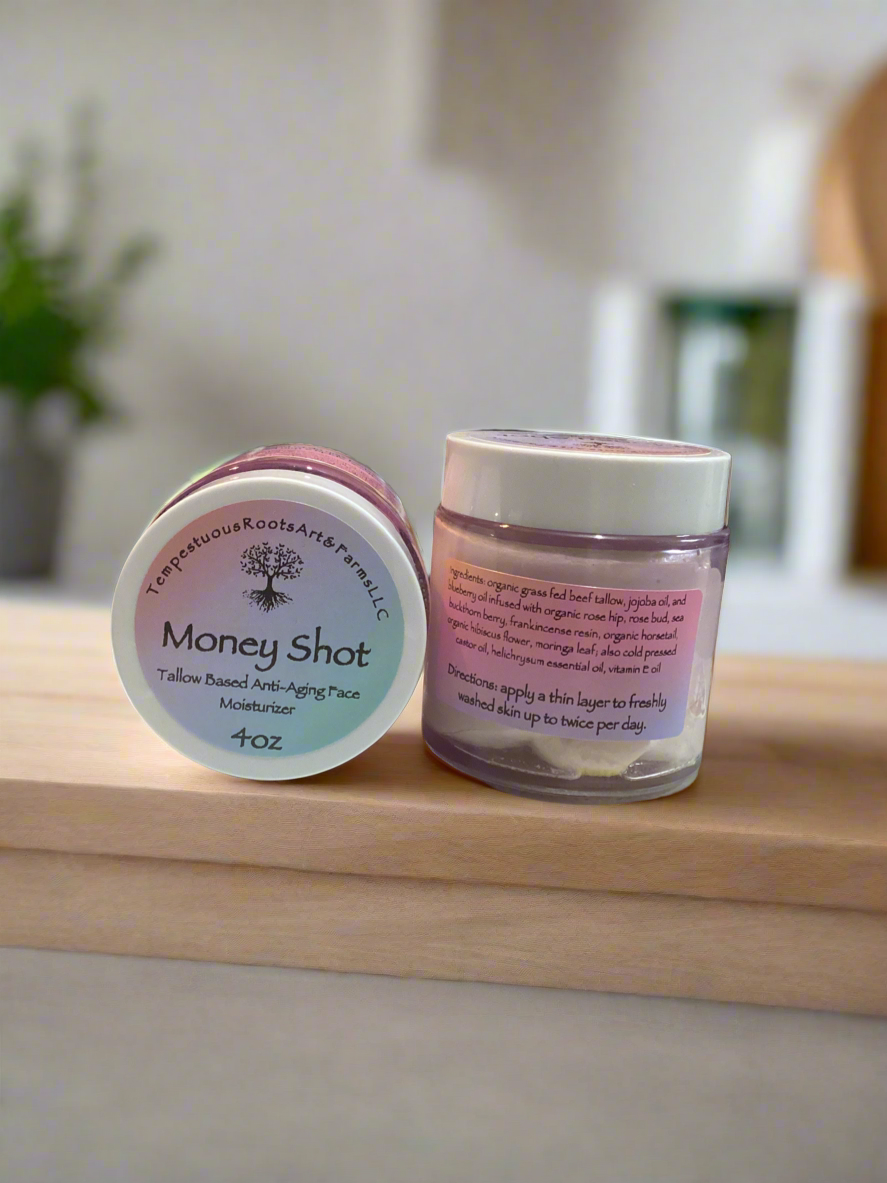 Two jars of 'Money Shot' anti-aging, all natural, face cream on a wooden surface with a blurred background