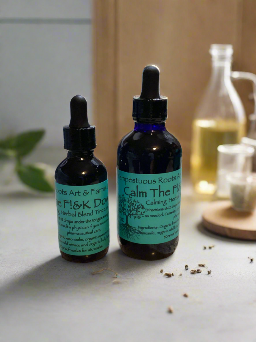 Herbal tincture in two dark glass bottles with dropper caps, one larger than the other, labeled 'Calm The F!&K Down!!' and positioned on a surface with a few dried leaves scattered around.