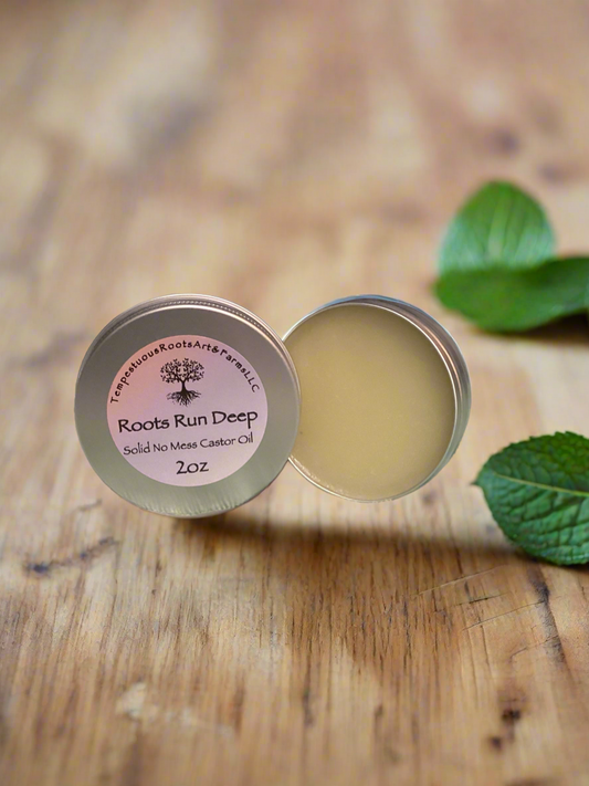 Solid no mess castor oil in a metal tin with 'Roots Run Deep' label on a wooden surface.