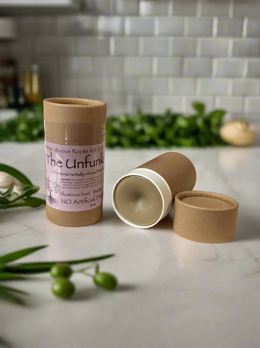 The image shows an all natural deodorant stick labeled 'The Unfunking' with its cap and base removed, displayed on a kitchen countertop with green olives and a rose in the background.