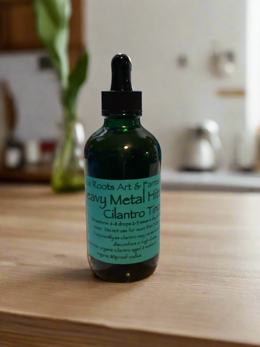A bottle of 'Heavy Metal Hitter'cilantro  tincture by Tempestuous Roots Art & Farms, with a dropper cap, placed on a kitchen counter.