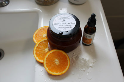 Zest The F!$K Up citrus cleaning scrub by Tempestuous Roots sitting on a white sink with orange slices and a dropper bottle